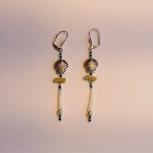 May include: A pair of silver earrings with a seashell charm, turquoise and black beads, and a white bone-like pendant.