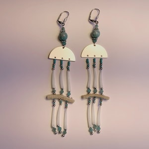 May include: A pair of long, dangling earrings with a gold crescent moon shape, turquoise beads, and white beads. The earrings are made with a silver wire and have a turquoise stone at the top.