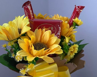May include: A bouquet of yellow sunflowers with a red box of Lindt chocolates and red chocolate bars in a brown paper gift bag with a yellow bow.