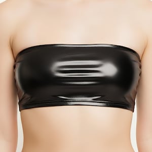 Puede incluir: Un top tubo negro brillante y sin tirantes. El top está hecho de un material liso y reflectante y lo lleva una persona. El top es de color negro liso y tiene un diseño sencillo y clásico. La prenda es un top corto.