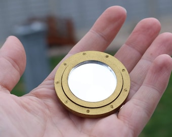 May include: A gold-colored round mirror with a circular frame that resembles a ship's porthole.
