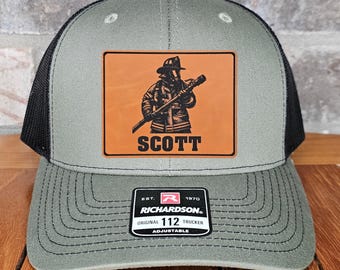 May include: A gray and black trucker hat with a firefighter graphic on a brown patch. The patch has the name "SCOTT" below the graphic. The hat is adjustable and has the "RICHARDSON" brand logo.