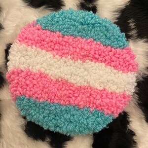 May include: A round, fluffy, crocheted wall hanging with a design of horizontal stripes in light blue, pink, and white.