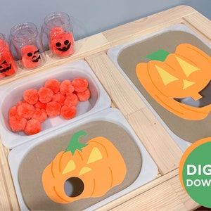 Puede incluir: Una mesa de actividades de madera con dos recortes de calabaza naranja con un agujero en el medio. La mesa tiene dos contenedores blancos, uno con pompones naranjas y el otro vacío. Hay tres frascos transparentes con pompones naranjas y caras de calabaza negras en el lateral. El texto "DESCARGA DIGITAL" está en un círculo verde en la esquina inferior derecha.