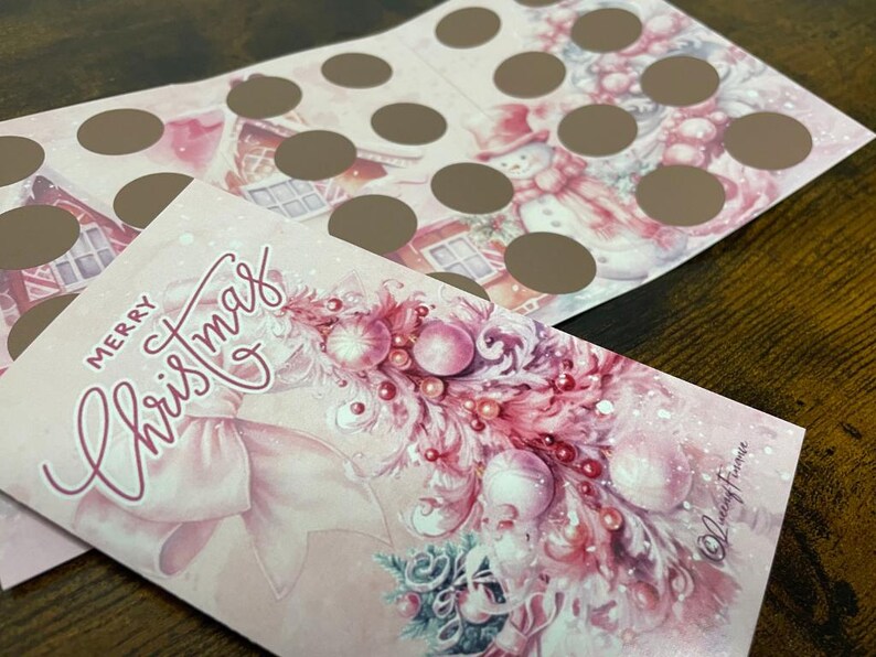 Pu&ograve; includere: Un biglietto di Natale rosa con un fiocco rosa e un albero di Natale rosa e bianco decorato con ornamenti. Il biglietto dice "Buon Natale" in scrittura rosa.