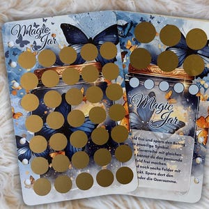 Könnte beinhalten: Zwei weiße Karten mit einem blauen und goldenen Design, das ein Glas mit Schmetterlingen zeigt. Der Text "Magic Jar" ist auf beiden Karten geschrieben. Die Karten haben goldene Kreise darauf.