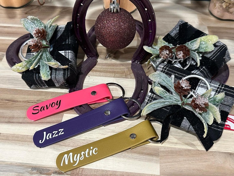 May include: Three black and white plaid gift boxes with pine cone and greenery accents, each with a different colored key chain attached. The key chains are labeled "Savoy", "Jazz", and "Mystic".