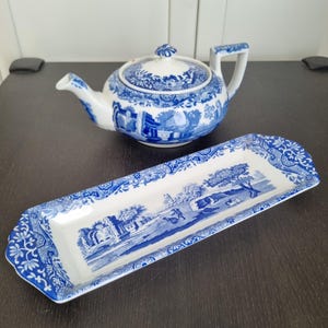Può includere: Una teiera e un vassoio da portata in porcellana blu e bianca con un motivo floreale. La teiera ha un coperchio e un manico. Il vassoio è rettangolare e ha un bordo rialzato.
