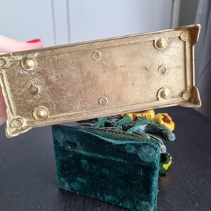 May include: A gold metal bookend with a green velvet base. The bookend features a sculpted design of sunflowers.