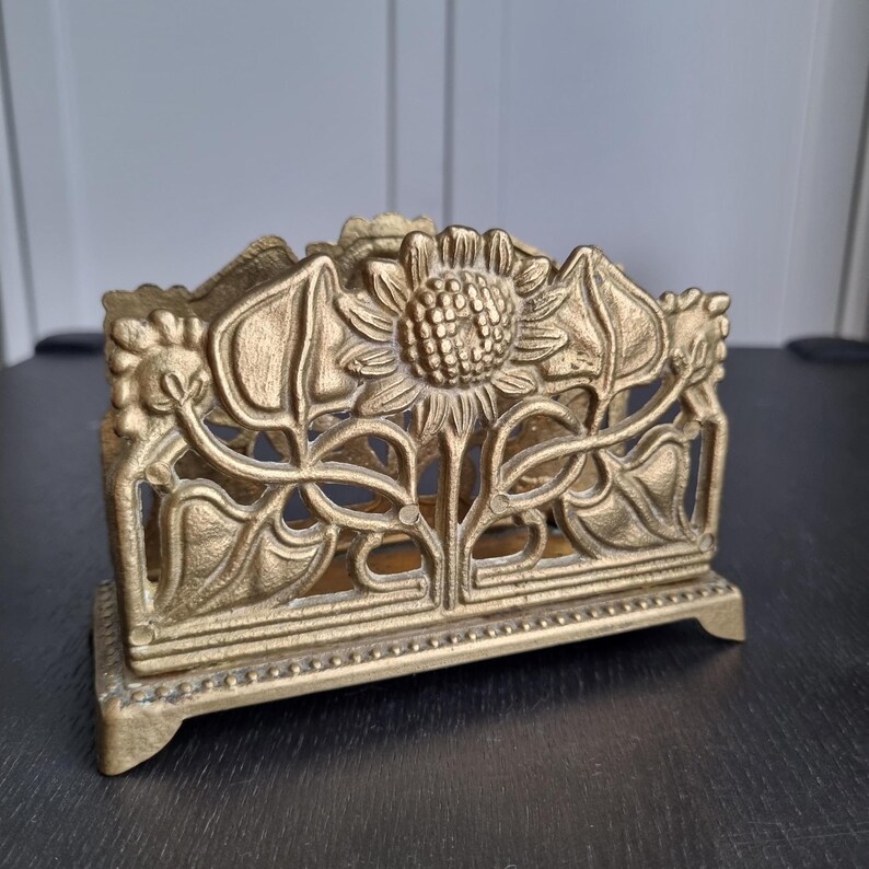 May include: Gold metal napkin holder with a sunflower and leaf design.
