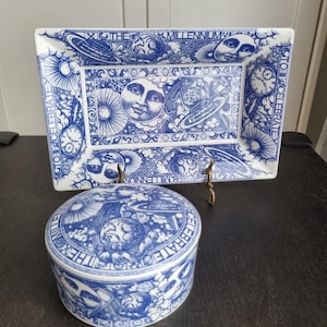 Könnte beinhalten: Ein blaues und weißes rechteckiges Tablett aus Keramik und eine runde Dose mit einem himmlischen Design. Das Tablett trägt den Text "The Millennium We Celebrate" und die Dose trägt den Text "The Millennium We Celebrate".