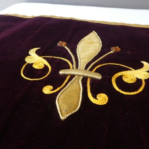 May include: A dark purple velvet pillow with a gold embroidered fleur-de-lis design.