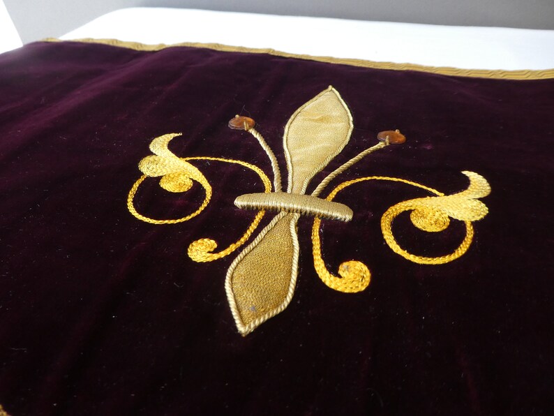 May include: A dark purple velvet pillow with a gold embroidered fleur-de-lis design.