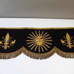 May include: A black velvet valance with gold embroidered details. The center features a heart with a cross and rays of light. The left and right sides have a fleur-de-lis design.