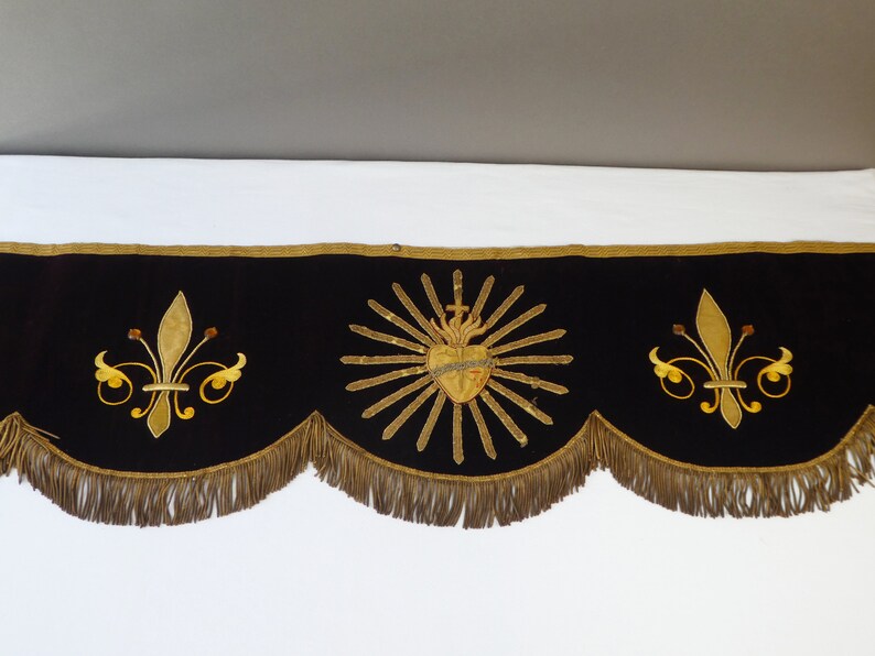 May include: A black velvet valance with gold embroidered details. The center features a heart with a cross and rays of light. The left and right sides have a fleur-de-lis design.