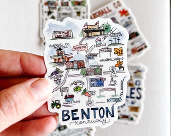 May include: A hand-drawn illustration of a map of Benton, Kentucky. The map features landmarks like the Mike Miller County Park, Marshall County Hospital, Kentucky Opry, and the Benton Drive-In. The map is in a watercolor style with a blue and white color scheme.