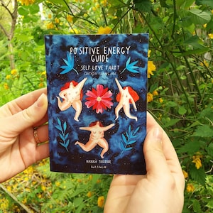 May include: A blue and black tarot deck guide with the title "Positive Energy Guide: Self Love Tarot Edition Française" and the authors Hanna Tricoire and Ewa Pawlak.