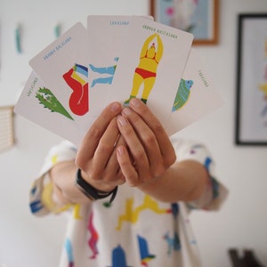 May include: A set of five cards with illustrations of yoga poses. The cards are white with colorful illustrations and text. The text on the cards includes the names of the poses: "Ananda Balasana", "Savasana", "Urhva Hastasana", "Tadasana", and "Vriksasana".