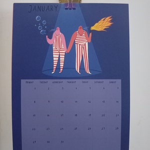 May include: A blue calendar with the word "JANUARY" at the top. The calendar features a cartoon illustration of two people in striped outfits, one blowing bubbles and the other holding a torch. The calendar grid shows the days of the month.