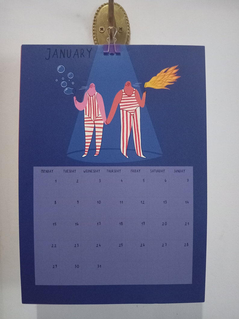 May include: A blue calendar with the word "JANUARY" at the top. The calendar features a cartoon illustration of two people in striped outfits, one blowing bubbles and the other holding a torch. The calendar grid shows the days of the month.