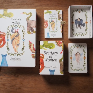 May include: A set of cards and a book titled "Bestiary of Women" by Hanna Tricoire and Katarzyna Jarosz. The cards feature illustrations of women with animal features, and the book has a similar design.