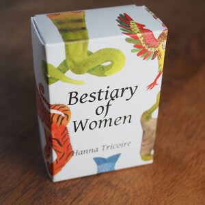 May include: A white box with colorful illustrations of animals, including a snake, a bird, and a tiger. The box is titled "Bestiary of Women" with the author's name, Hanna Tricoire, printed below.
