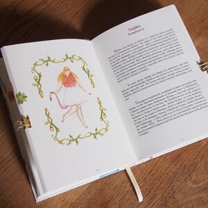 May include: An open book with a watercolor illustration of a woman with blonde hair wearing a red top and white skirt. The text on the page reads "Huldra Scandinavia".