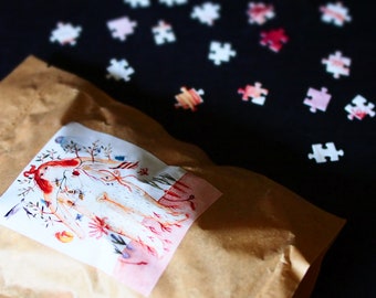 Puede incluir: Una bolsa de papel marrón con una ilustración colorida de una mujer y un perro en un entorno de bosque. La bolsa está rodeada de piezas de rompecabezas dispersas sobre un fondo negro.