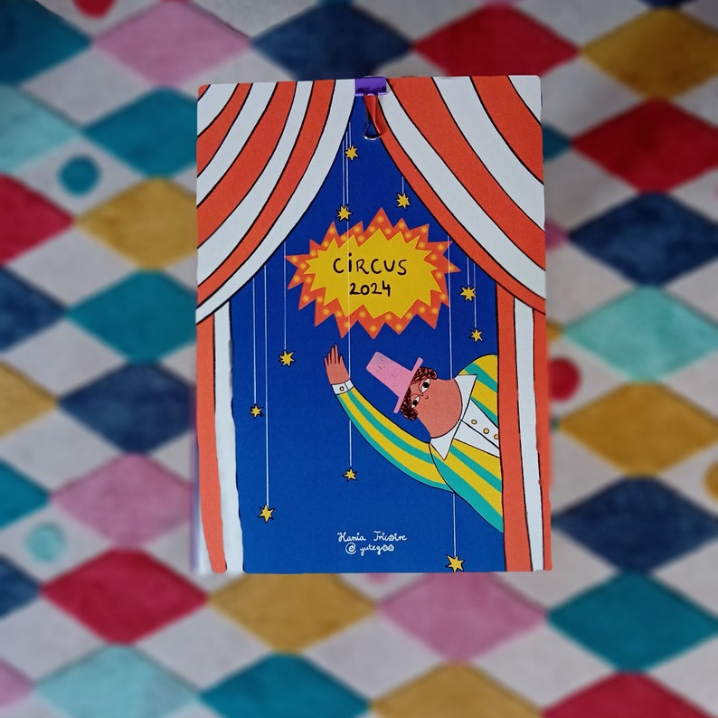 May include: A blue and yellow circus themed calendar with a red and white striped tent. The calendar features a cartoon clown with a pink hat and a yellow and green striped shirt. The text "CIRCUS 2024" is in a yellow starburst.