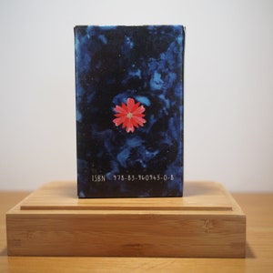 Puede incluir: Un libro azul con una flor roja en la portada. El libro tiene el texto "ISBN 978-83-960943-0-8" en la parte inferior.