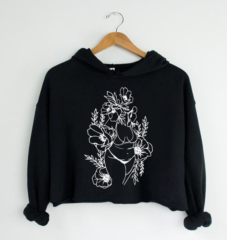May include: Black cropped hoodie with a white outline of a woman's body surrounded by flowers.