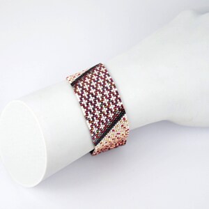 Pode incluir: Um bracelete de contas com um padr&atilde;o geom&eacute;trico em tons de vermelho, branco e preto.