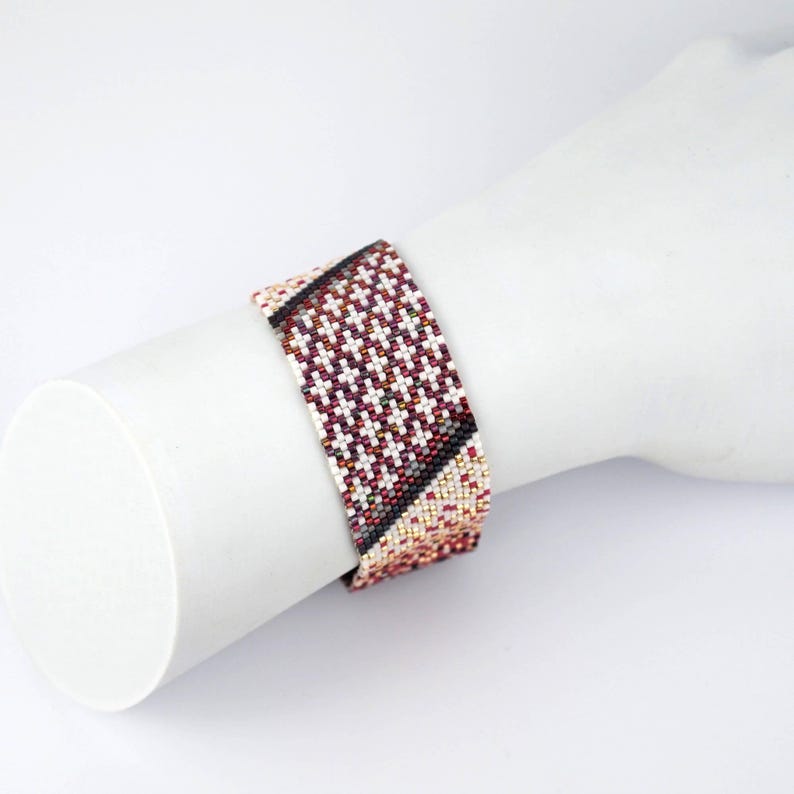 Pode incluir: Um bracelete de contas com um padr&atilde;o geom&eacute;trico em tons de vermelho, branco e preto.