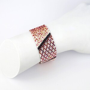 Pode incluir: Um bracelete de contas com um padr&atilde;o geom&eacute;trico em tons de vermelho, branco, dourado e preto.