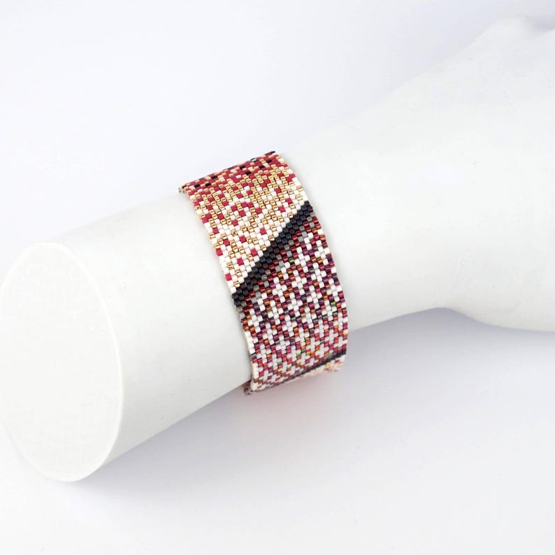 Pode incluir: Um bracelete de contas com um padr&atilde;o geom&eacute;trico em tons de vermelho, branco, dourado e preto.