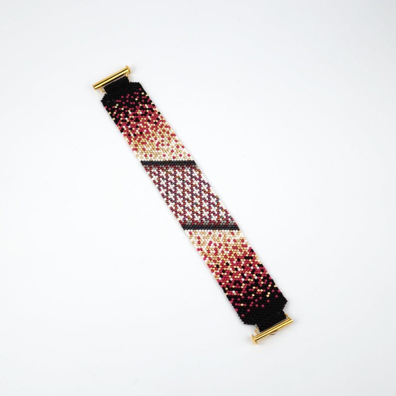 Pode incluir: Um bracelete de contas com um design degrad&ecirc; em preto, branco e rosa. O bracelete tem fechos dourados.