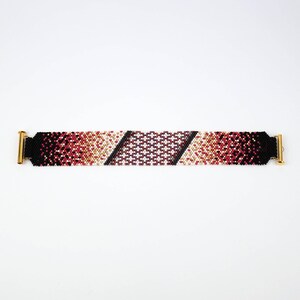 Pode incluir: Um bracelete de contas com um padr&atilde;o degrad&ecirc; de contas pretas, vermelhas, brancas e douradas. O bracelete tem fechos de metal dourado em cada extremidade.