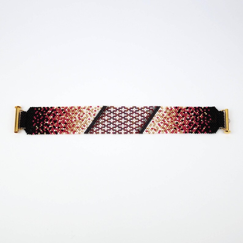 Pode incluir: Um bracelete de contas com um padr&atilde;o degrad&ecirc; de contas pretas, vermelhas, brancas e douradas. O bracelete tem fechos de metal dourado em cada extremidade.