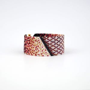 Pode incluir: Um bracelete de contas com um padr&atilde;o geom&eacute;trico em tons de vermelho, branco, dourado e preto.