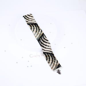K&ouml;nnte beinhalten: Ein schwarz-wei&szlig;es Armband aus Perlen mit Zebra-Muster. Das Armband hat einen silbernen Verschluss.