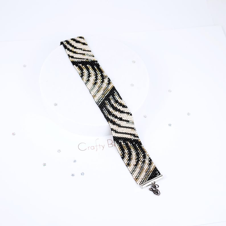 K&ouml;nnte beinhalten: Ein schwarz-wei&szlig;es Armband aus Perlen mit Zebra-Muster. Das Armband hat einen silbernen Verschluss.