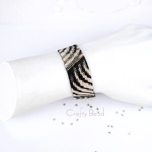 K&ouml;nnte beinhalten: Ein schwarz-wei&szlig;es Armband aus Perlen mit Zebra-Muster. Das Armband befindet sich am Handgelenk.