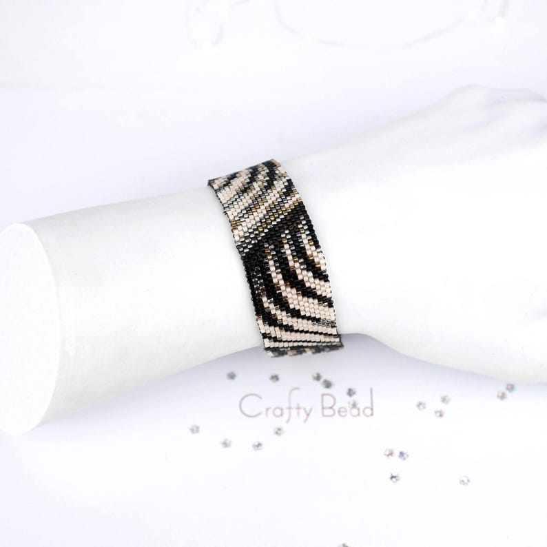K&ouml;nnte beinhalten: Ein schwarz-wei&szlig;es Armband aus Perlen mit Zebra-Muster. Das Armband befindet sich am Handgelenk.