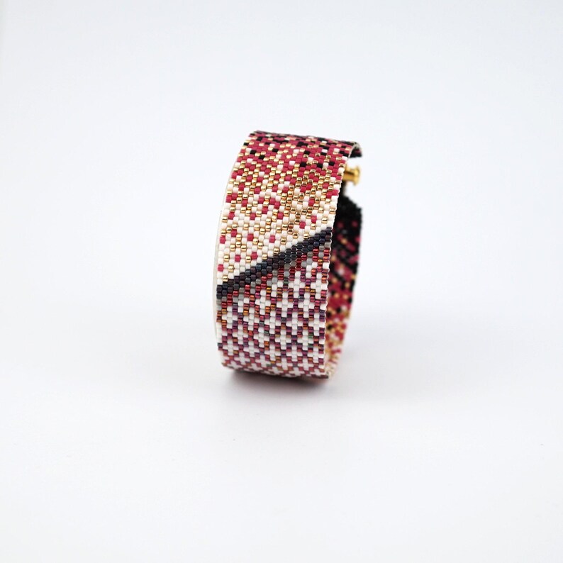 Pode incluir: Um bracelete de contas com um padr&atilde;o geom&eacute;trico em tons de vermelho, branco, preto e dourado.
