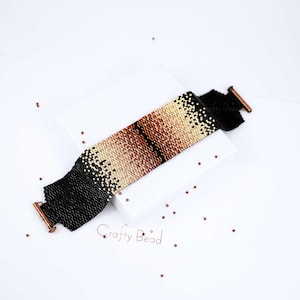 Op de afbeelding: Een zwarte en bruine kralenarmband met een verloopmotief. De armband heeft koperen sluitingen en ligt op een wit oppervlak.