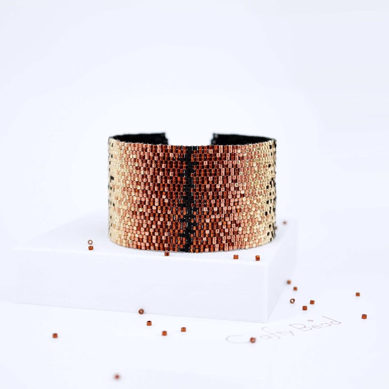 Op de afbeelding: Een kralen armband met een gradi&euml;nt van goud, koper en bruine kleuren. De armband heeft een zwarte streep in het midden.