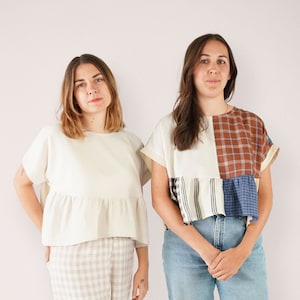 Op de afbeelding: Twee mensen in casual kleding. De persoon links draagt een wit topje met een gerimpelde zoom en een beige en witte geruite broek. De persoon rechts draagt een veelkleurig patchwork topje met een blauwe spijkerbroek.