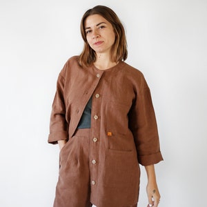 May include: A brown linen jumpsuit with a button-up front and two large pockets. The jumpsuit has a relaxed fit and is made of a lightweight fabric.
