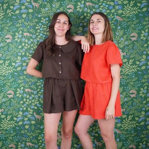 May include: Two people wearing matching outfits. The person on the left is wearing a brown linen top with a peter pan collar and matching shorts. The person on the right is wearing a bright orange linen top with matching shorts. Both outfits have short sleeves.