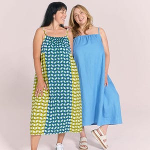 May include: Two women in summer dresses. One is a solid light blue, the other has a geometric pattern in green, blue and white. Both dresses have thin straps and reach the mid-calf. The women are smiling.